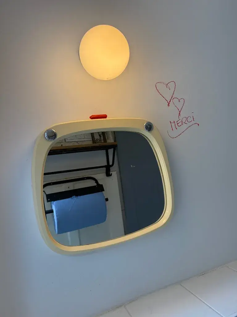 Ein runder Spiegel an der Wand, daneben mit Lippenstift geschrieben: Merci