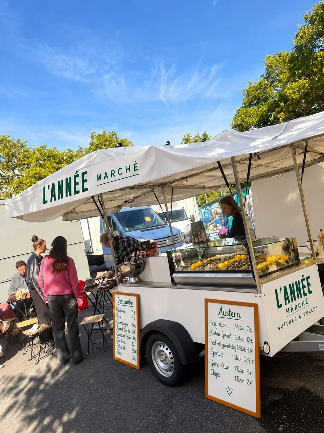 Der weiße Marché-Anhänger mit Sonnendach und Kreidetafeln auf dem Wochenmarkt